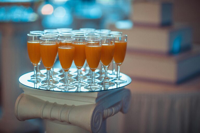 A collection of orange juice glasses elegantly displayed on a pillar at an indoor event.